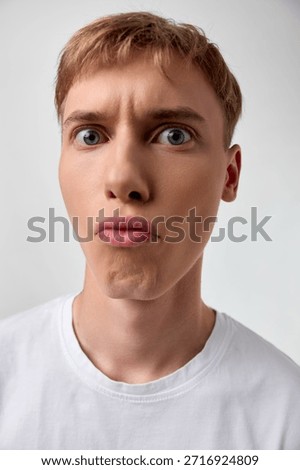 Puzzled expression on a closeup of a young man, wide eyes and pursed lips, capturing surprise, confusion, and curiosity in a simple studio setting for expressive stock imagery