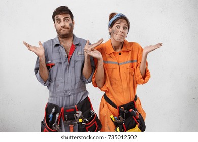 Puzzled Female And Male Plumbers Can`t Understand Where Breakage Is, Shrug Shoulders In Bewilderment, Have Dirty Faces. Two Young Technicians Being Confused As Repair Leakage Or Brocken Tube