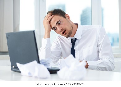 Puzzled look of stress man at work open laptop and crumpled sheet of paper
