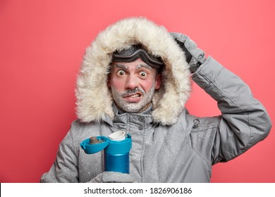 Puzzled Male Hiker Has Frozen Face Shocked By Cold Conditions In Expedition Wears Warm Jacket And Ski Goggles Drinks Hot Beverage Poses Indoor Against Vivid Rosy Background. Lifestyle Snowboarding