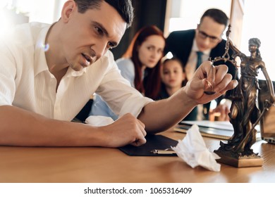 Puzzled man puts engagement ring on scales of figure of Themis next to agitated woman hugging girl. Adult couple is divorced. Couple divorce.