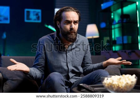 Puzzled person on couch using TV to binge thriller series on subscription based streaming services, disagreeing with characters. Man watching VOD shows on television display, feeling confused by plot
