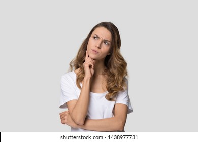 Puzzled thoughtful young woman touching chin, attractive doubtful female making decision, looking aside, pensive client customer pondering shopping offer, isolated on studio background
