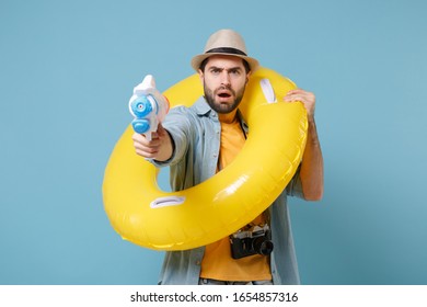 Puzzled traveler tourist man in yellow clothes with photo camera isolated on blue background. Passenger traveling abroad on weekends. Air flight journey concept. Hold inflatable ring toy water gun - Shutterstock ID 1654857316