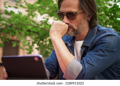 Puzzled Up, Sad Middle Aged Man Working Outdoors Using Digital Tablet. Handsome Freelancer Traveling Man Not Happy Checking Work Or Social Media Sitting At City Street Cafe. 