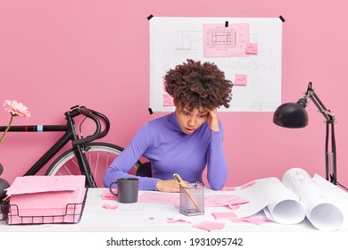 Puzzled woman architect improves graphics corrects mistakes busy working on archiectural project and having deadline poses at desktop has deadline surrounded with papers tries to solve problem