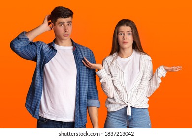 Puzzled young couple do not understand what happening or does something wrong. Surprised man scratches back of his head, sad woman spreads her arms to sides isolated on orange background, free space