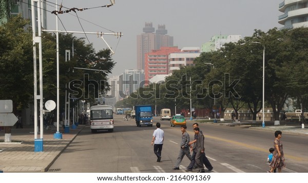 Pyongyang, North Korea,\
09.09.2017: view of a wide street with a few cars and people\
passing through it in the background high-rise colorful buildings\
in pjongjang