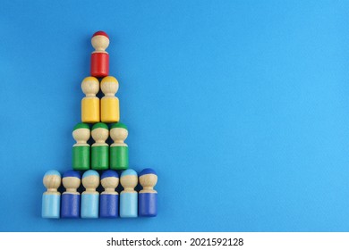 Pyramid Of Multicolored Wooden Toy People On Blue Background With Copy Space, Concept Of Social Rating Or Class Inequality And Wealth Rating Or Company Business Structure 