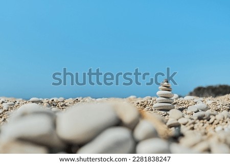Pyramid stones balance on the beach against a blue bright sky. Object in focus, blurred background, idea of a vacation or retweet by the sea