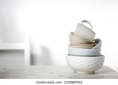 A pyramid of white bowls, plates, and cups of different sizes and colors on a beige table in the kitchen. Scandinavian style. A place for your text. Copy space - Shutterstock ID 2120809352