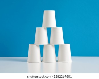 Pyramid of white paper cups on blue background.