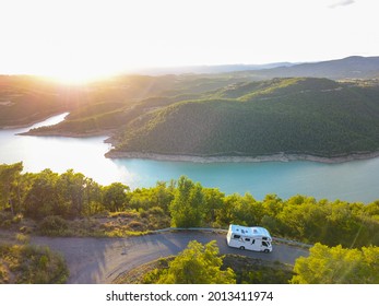 Pyrenees, Spain; 07-17-2021: Aerial drone view of a van or caravan driving at sunset with a blue lake at the back.