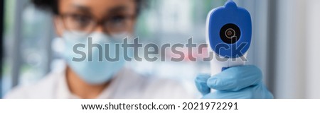 Pyrometer in hand of african american doctor on blurred background, banner