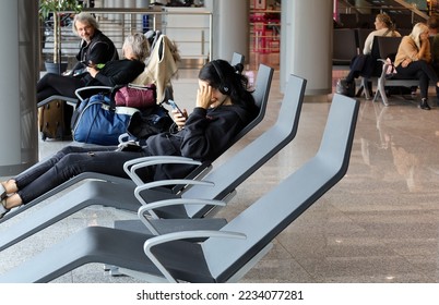 Pyrzowice, Poland - September 2022: A young woman with headphones and a smartphone resting in a relax zone at departure waiting hall at the Pyrzowice Airport. Selected focus. - Shutterstock ID 2234077281
