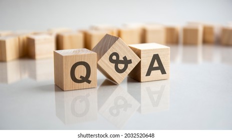 Q and A - an abbreviation of wooden blocks with letters on a gray background. Reflection of the Q and A caption on the mirrored surface of the table. Selective focus.