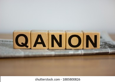 Q Anon symbol. Cubes placed on a newspaper with the word 'QANON'. Beautiful wooden table. White background. Business and Q Anon concept. Copy space.