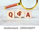 Q and A questions and answers symbol. Concept words Q and A on wooden cubes with a magnifying glass in the background