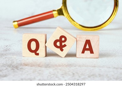 Q and A questions and answers symbol. Concept words Q and A on wooden cubes with a magnifying glass in the background