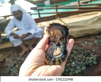 Qatar, Doha, December 11, 2019: Open Seashell With Black Pearls In Woman Hand With A Fishing Boat And Arabian Man Background