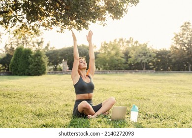 Qigong chinese meditation online with laptop in green park. Sport training outdoor. Fit asian girl is meditating outside