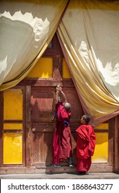 Qinghai, China. Aug 8, 2009. Two young Tibetan Buddhist lamas wear red traditional robes. The little boy stands on tiptoe to help the temple lock the wooden door.