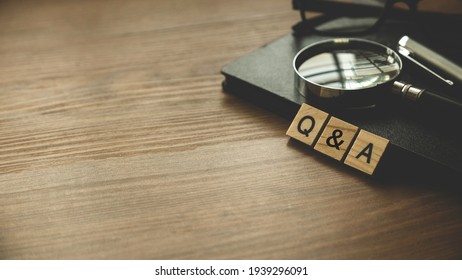 QnA or questions and answers concept .Selective focus of wooden alphabet ,glasses, notebook and magnifying glass on wooden background with copy space.
