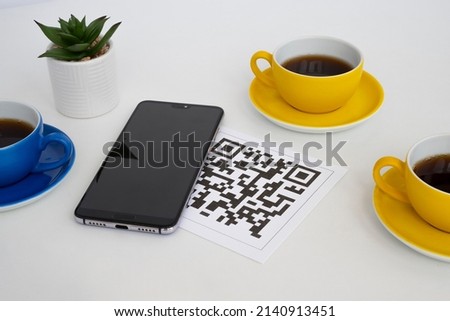 QR code for online menu service at table in restaurant New contactless technology lifestyle protect. Phone and blue and yellow mugs on the table