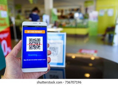 QR code payment, cashless technology concept : Man's left hand holds a touch screen smartphone scans QR code to pay money in a retail shop. QR code is a matrix barcode stores informations of an item. - Powered by Shutterstock