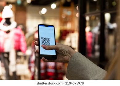 QR code in a smartphone in a woman's hand in a clothing store in a shopping mall. Green pass for lifestyle during a pandemic. Close-up.