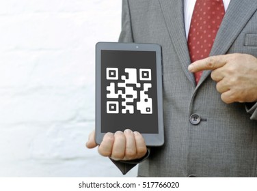 Qrcode icon on the tablet screen. Businessman points finger at qr code icon on the tablet PC. Identification of goods and services by scanning qrcode.
