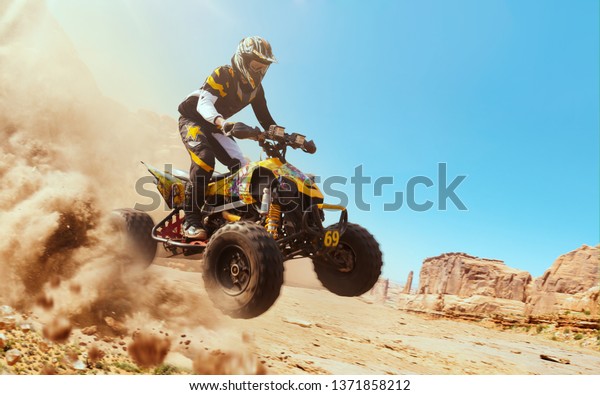 Quad bike in dust cloud, sand quarry on\
background. ATV Rider in the\
action.