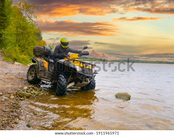 Quad bike\
on the river bank. The ATV driver drove into water. Quad bike on\
the background sunset. A man travels on a quad bike. A yellow ATV\
stands in lake. Concept - outdoor\
activity.