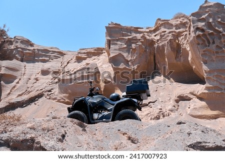 Quad bike parked on the seafront near the sandy beach of Monolithos on Santorini island, Greece. The coasts in this area resemble lunar-shaped landscapes. Travel, relaxation, adventure.