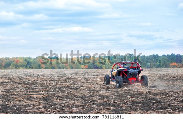 Quad bike was taken from behind. Red buggy in a\
plowed field against the background of autumn trees. concept of\
power speed and freedom.