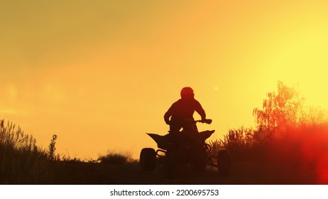 Quad biker jumping in sunset, silhouette with falling sun on horizon.