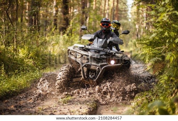 a quad\
moving trough the mud with two riders on\
it
