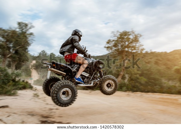 The quad racer is jumping on the dusty\
road. Quad bike off-road. Quad bike in\
action.