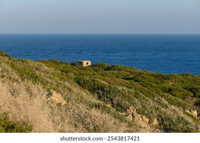 A quaint building hides among rolling hills, offering breathtaking views of the endless ocean at sunset. - Powered by Shutterstock