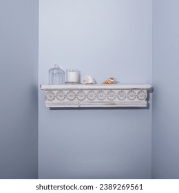 A quaint and decorative white wall shelf with a distressed finish and carved flower details, adorned with a candle, glass dome, and seashell - Powered by Shutterstock