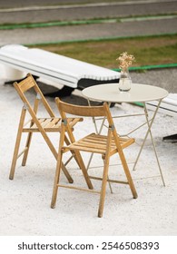 A quaint outdoor setup featuring two wooden chairs and a round table with a small vase of flowers, perfect for relaxation in a peaceful area.