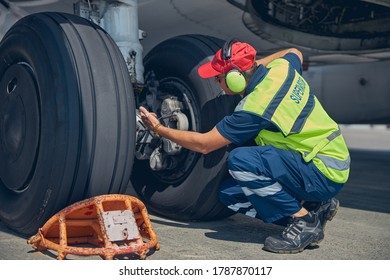 Qualified aircraft mechanic in workwear performing a visual inspection of the airplane landing gear system - Powered by Shutterstock