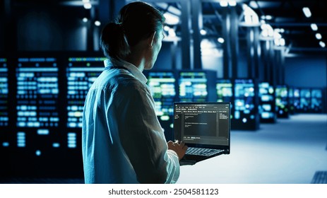 Qualified IT developer running code on laptop, troubleshooting and upgrading data center equipment designed to accommodate server cabinets, networking systems and storage arrays