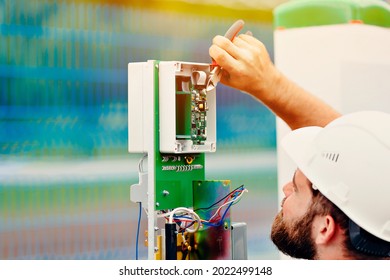 A qualified electrical engineer sets up a control and measuring device at an industrial facility on a summer day. Specialist power engineer in helmet and uniform at work. An authentic portrait.