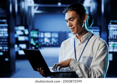 Qualified engineer in data center using laptop to prevent system overload during peak traffic periods. Diligent worker in server room ensuring there is enough network bandwidth for smooth operations