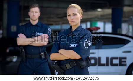 Qualified police officers posing on background of patrol car, criminal justice