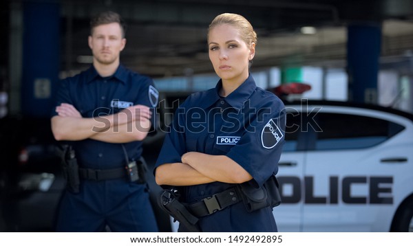 Qualified police officers posing on background of\
patrol car, criminal\
justice