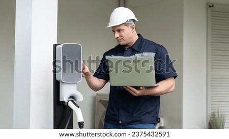 Qualified technician working on home EV charging station installation, making troubleshooting and configuration setup on charging system with laptop for EV at home. Panorama Synchronos Foto stock © 