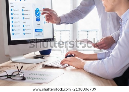 Quality Assurance (QA) and Control (QC) management. Standardization and certification concept. Compliance to international ISO standards. Manager and auditor looking at certificate on computer screen.