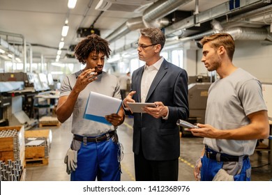 Quality control inspector and metal processing plant worker discussing while going through paperwork and using touchpad in a factory.  - Powered by Shutterstock